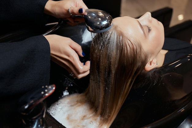 Kapper in schoonheidssalon wast het haar van zijn klant vóór de procedure voor het aanbrengen van natuurlijke herstellende ingrediënten en vitamines op haar en kapsel