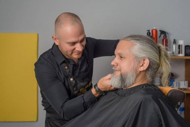 Kapper knippen en stylen van de baard van een grijsharige man B Kapperszaak voor mannen