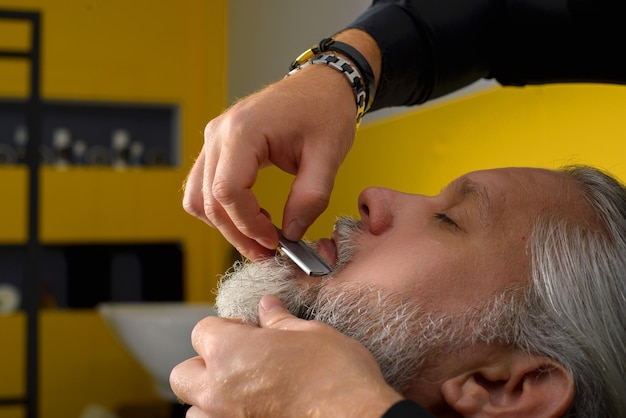 Kapper knippen en stylen van de baard van een man met grijs haar Baardknippen en stylen