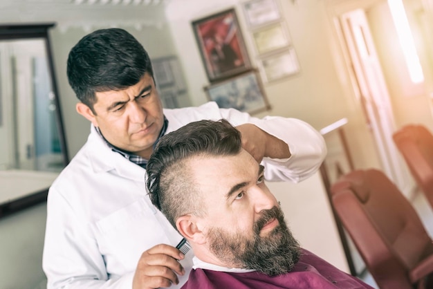 Kapper maakt een mohawk-kapsel naar de volwassen man met baard