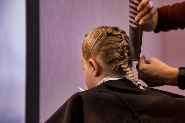 Kapper maakt kapsel voor baby in kapperszaak close-up Kapper vrouw maken modieuze vlechten kapsel voor schattig klein blond meisje kind