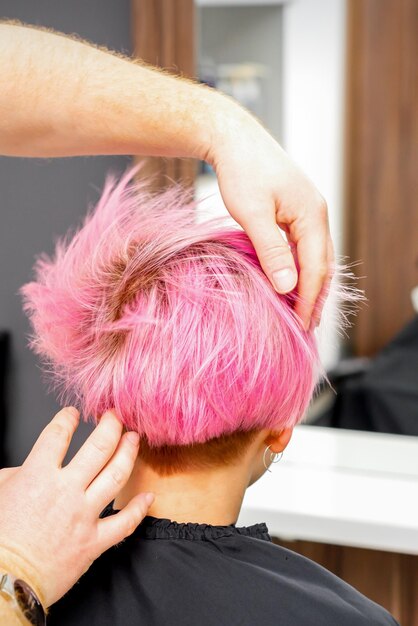 Kapper met handen controleert en repareert het korte roze kapsel van de jonge blanke vrouw in een kapsalon