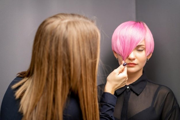 Kapper met handen controleert en repareert het korte roze kapsel van de jonge blanke vrouw in een kapsalon