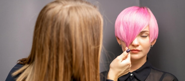 Kapper met handen controleert en repareert het korte roze kapsel van de jonge blanke vrouw in een kapsalon