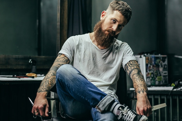 kapper met lange baard en tatoeages zitten met instrumenten