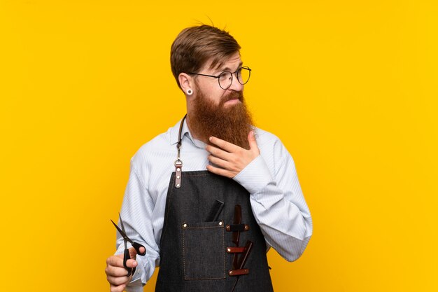 Kapper met lange baard in een schort over geïsoleerde gele een idee denken en muur die kant kijken