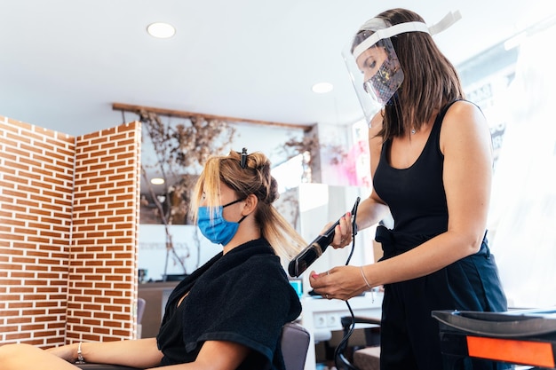 Kapper met masker die het haar van een vrouw strijkt