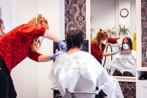 Kapper met masker en handschoenen die de uiteinden met een schaar naar de klant knippen