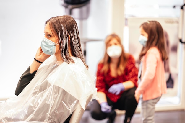 Kapper met masker en handschoenen in gesprek met de dochter van de klant