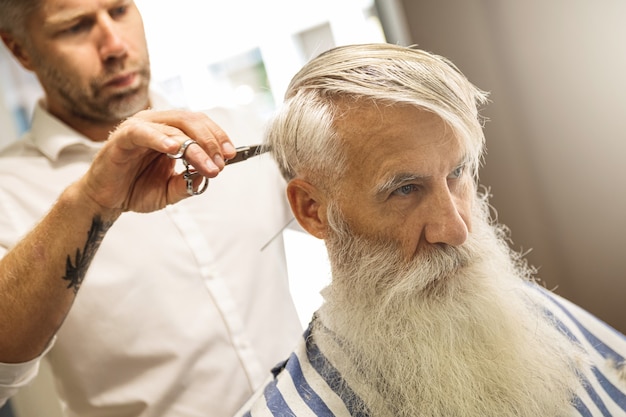 Kapper stijlvolle kapsel maken voor een knappe oude man in de kapperszaak