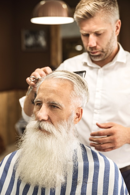 Kapper stijlvolle kapsel maken voor een knappe oude man in de kapperszaak