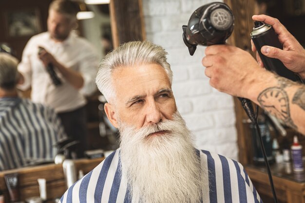 Kapper stijlvolle kapsel maken voor een knappe oude man in de kapperszaak