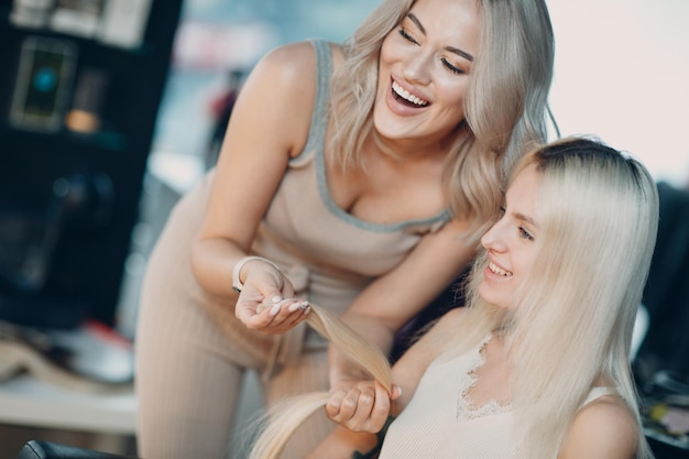 Kapper vrouw haarverlengingen maken aan jonge vrouw met blonde haren in schoonheidssalon. Professioneel haarverlengingsconcept