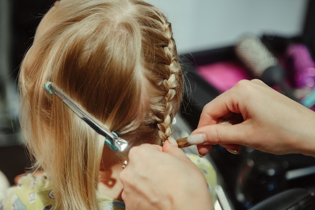 Kapper vrouw maakt modieus mooi kapsel voor schattig klein blond meisje kind in moderne kapperszaak, kapsalon. kapper maakt kapsel voor jonge baby in kapperszaak. concept kapsel en schoonheid