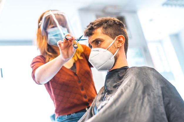 Kappers na de pandemie van het Coronavirus. Kapper met gezichtsmasker en beschermend scherm, covid-19. Sociale afstand, nieuwe normaliteit