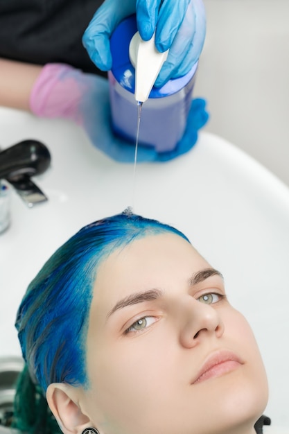 Kappershanden knijpt shampoo en conditioner uit tube in hoofd van vrouw met blauw haar