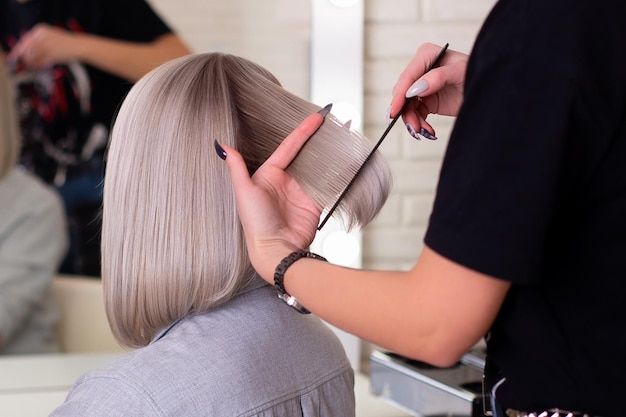 Kappershanden met borstel en schaar die blond haar knippen in schoonheidssalon