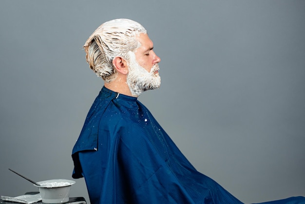 Kapperszaak. Portret van bebaarde man kleur haar. Proces van een man haarkleuring bij kapsalon.