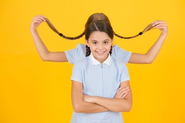 Kapsalon. Vrolijke schoolmeisjes gele achtergrond. Kleine meisjes spelen met schattige vlechten. Mooie schoolmeisjes. Terug naar schoolconcept. Leuke schoolmeisjes. Meisjes met gevlochten kapsel.