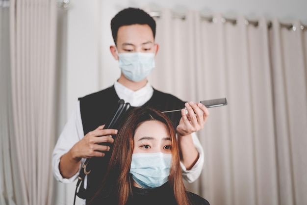 Kapsalonconcept zowel mannelijke haarstylist als vrouwelijke klant die een beschermend gezichtsmasker draagt tijdens het kapselproces.