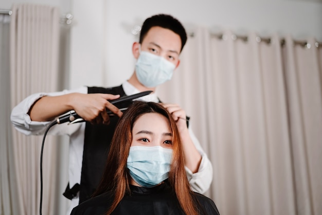 Kapsalonconcept zowel mannelijke haarstylist als vrouwelijke klant die een beschermend gezichtsmasker draagt tijdens het kapselproces.