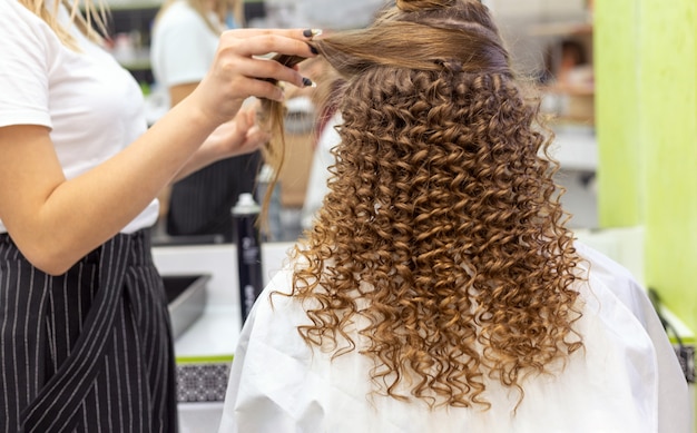 Kapsel achteraanzicht. Kapper die kapsel maakt aan rode blonde haarvrouw met lang haar in schoonheidssalon