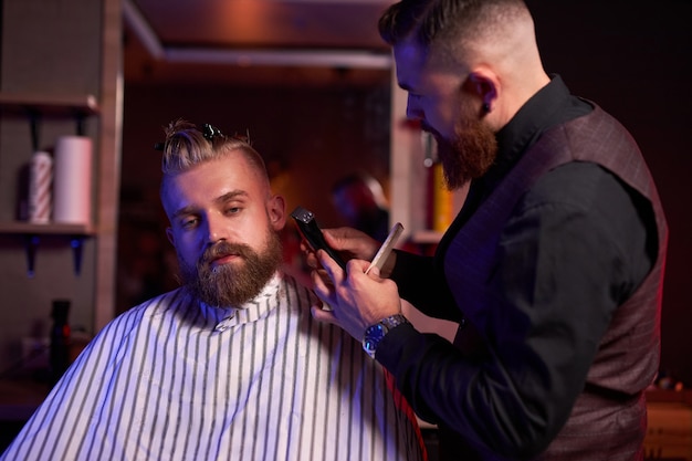 Kapsel bij de kapper, in de salon. kapper man knipt het haar op het hoofd van de knappe jonge cliënt