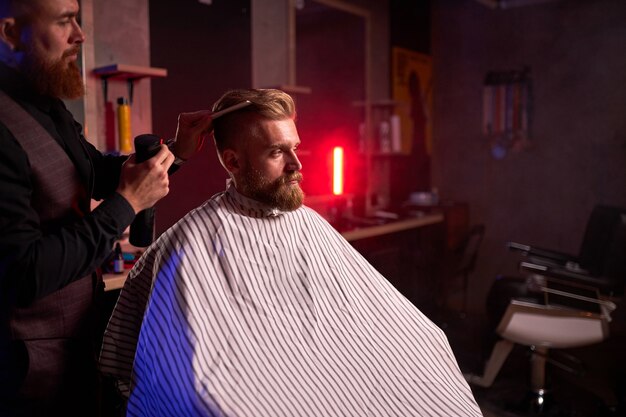 Kapsel bij de kapper, in de salon. kapper man knipt het haar op het hoofd van de knappe jonge cliënt