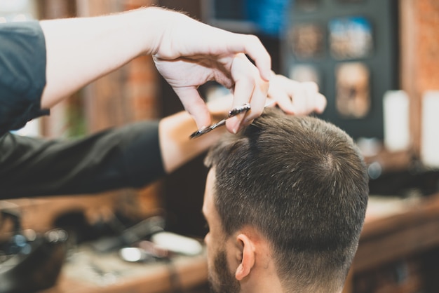 Kapsel bij de kapper. Kapper knipt het haar op het hoofd van de cliënt. Het proces van het creëren van kapsels voor mannen. Een man in een herenkapper. Het nabije plan. Apparatuurstylist. Selectieve aandacht