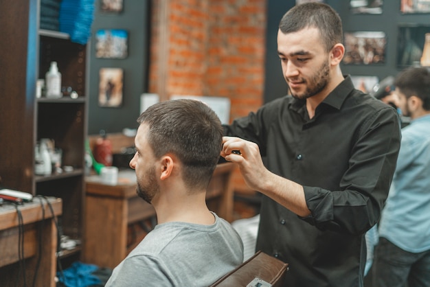 Kapsel bij de kapper. kapper knipt het haar op het hoofd van de cliënt. het proces van het creëren van kapsels voor mannen. een man in een herenkapper. het nabije plan. apparatuurstylist. selectieve aandacht