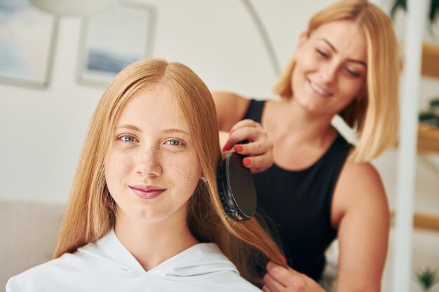 Kapsel doen Vrouwelijke tiener met haar moeder is overdag thuis