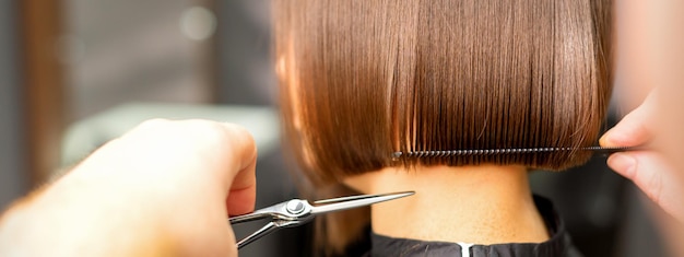 Kapsel van kort haar van jonge blanke vrouw door handen van een kapper in een achteraanzicht van een kapsalon close-up