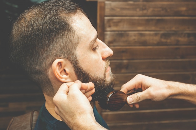 Kapselhoofd en baard in een herenkapper. Kapper trekt de baard van de klant aan en kamt deze. Proces van het maken van een kapsel en het stylen van een baard voor mannen. Man in een herenkapper. Apparatuurstylist. Selectieve aandacht