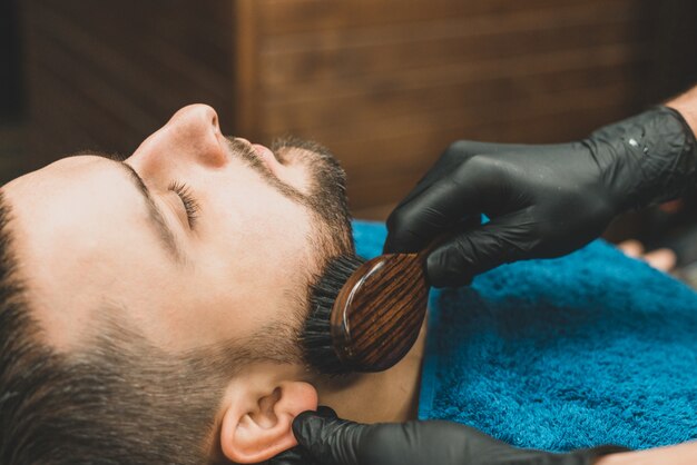 Kapselhoofd en baard in een herenkapper. Kapper trekt de baard van de klant aan en kamt deze. Proces van het maken van een kapsel en het stylen van een baard voor mannen. Man in een herenkapper. Apparatuurstylist. Selectieve aandacht