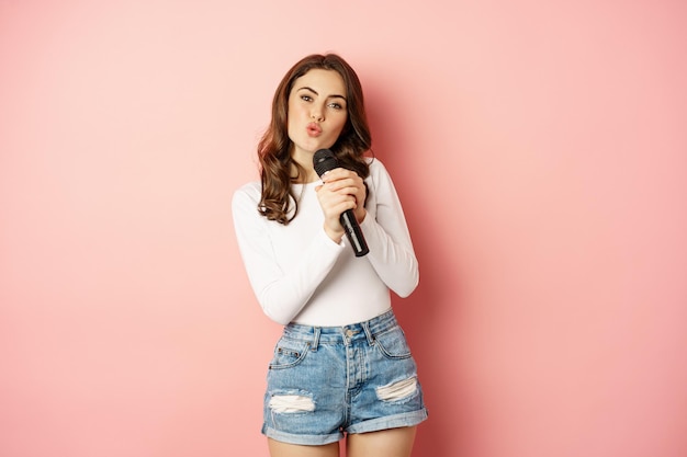 Karaoke. gelukkig lachend meisje zingen in de microfoon, dansen en plezier hebben, staande over roze achtergrond