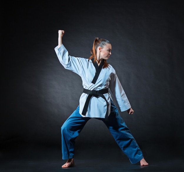 La ragazza di karate in kimono bianco e karate formazione cintura nera su sfondo grigio.