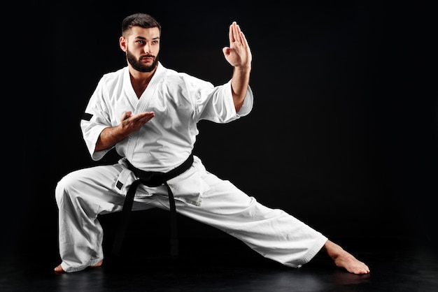 Karate man in een kimono in vechthouding op een zwarte achtergrond