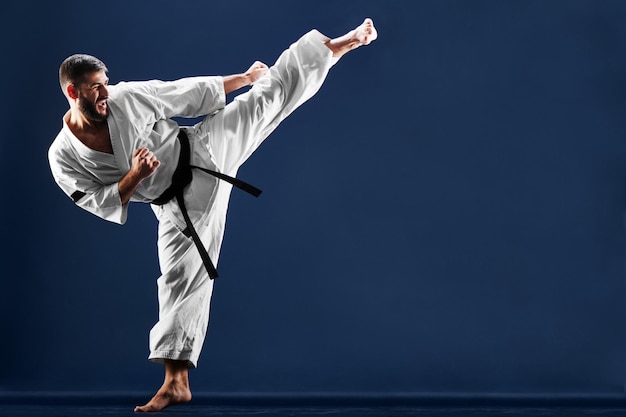 Karate man in a kimono hits foot on a blue background