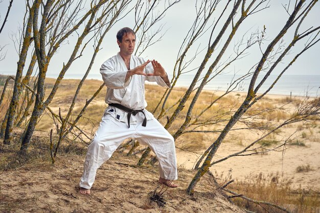 Foto uomo di karate con un vecchio kimono e cintura nera che si allena sulla riva del mare concetto di arti marziali