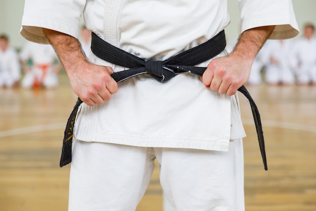 Photo karate master in a white kimono and with a black belt, stands in front of the formation of his students. martial arts school in training in the gym.