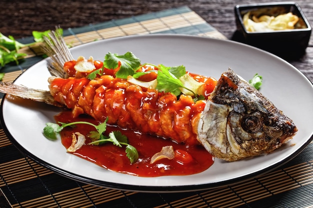 Karpereekhoorn: chinese zoetzure vis met verse koriander en gedroogde knoflook bovenop geserveerd op een grijze plaat op een donkere oude houten tafel, bovenaanzicht, close-up