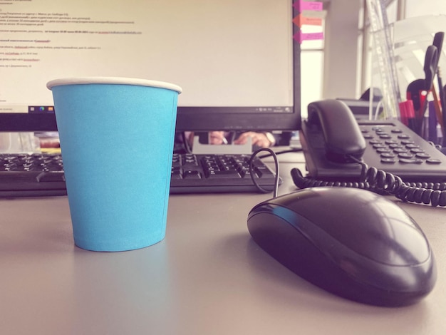 Foto kartonnen blauwe koffiebeker uit een coffeeshop op een desktop met een computer met toetsenbord