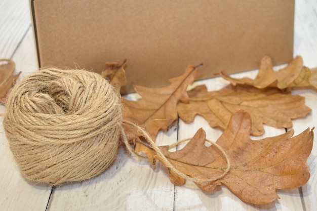 Kartonnen doos, herfstbladeren en bal van touw op de achtergrond van houten tafelblad. seizoenslevering