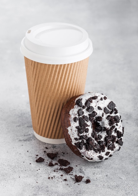 Kartonnen koffiekopje met zwarte koekjes donut op stenen keuken. Cafe drankje en snack.