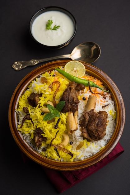 Kashmir montone gosht o agnello biryani preparato con riso basmati servito con salsa di yogurt su sfondo lunatico, messa a fuoco selettiva