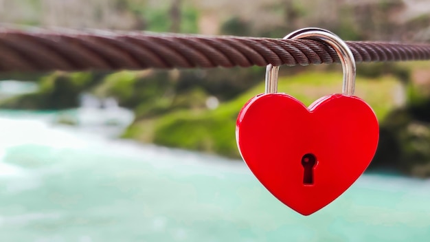 Kasteel in de vorm van een rood hart hangt aan een metalen kabel tegen de achtergrond van de rivier en de natuur