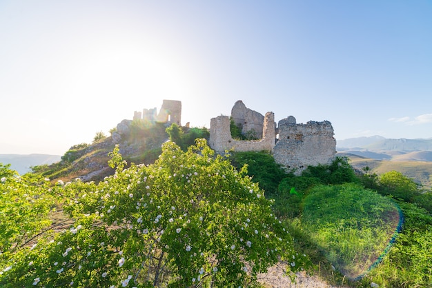 Kasteelruïnes op de bergtop bij rocca calascio, italiaanse reisbestemming, mijlpaal in het gran sasso national park, abruzzo, italië. helderblauwe lucht zon barstte in tegenlicht