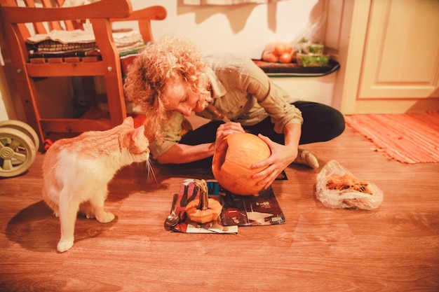 Foto kat door vrouw die pompoen snijdt thuis tijdens halloween