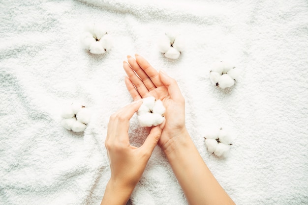 Katoenen bloemen in een vrouwelijke elegante hand met manicure op een muur van een witte badstofhanddoek