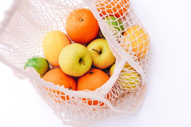 Katoenen mesh tas met vers kleurrijk fruit op lichte achtergrond, close-up. Geen afvalconcept